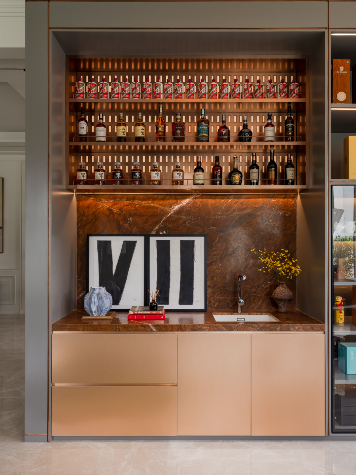 The wine collection is arranged on lit shelving above a marble-topped bar counter with a built-in sink