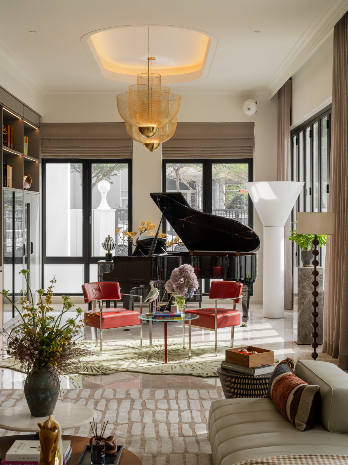 A brass mesh chandelier hangs above a seating area with red leather-and-chrome chairs, set beside the grand piano