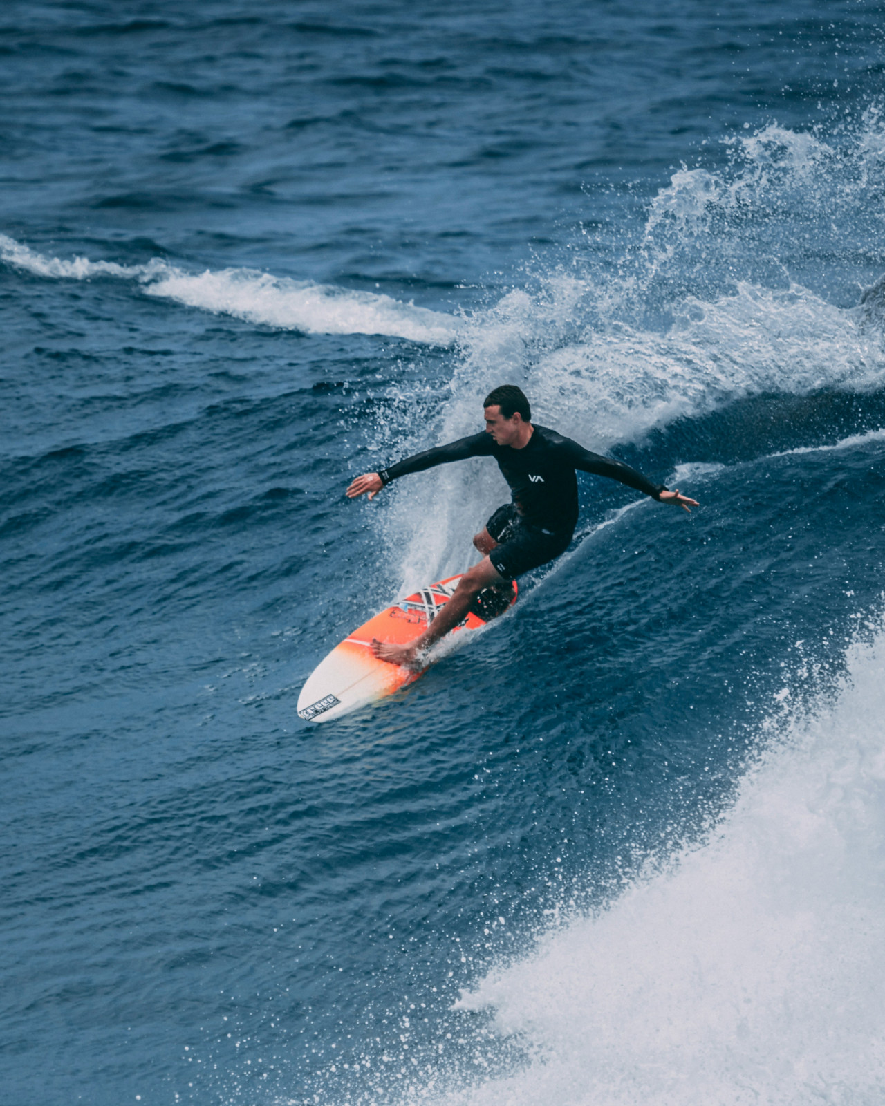 A surfer in a black wetsuit rides an ocean wave, highlighting the region's vibrant watersports culture ahead of the Asian Games.