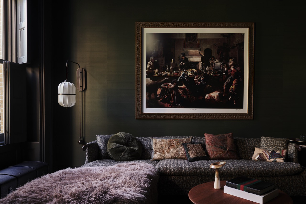 A dark, richly upholstered sitting area beneath a framed photograph, with a sheepskin throw and layered textile cushions