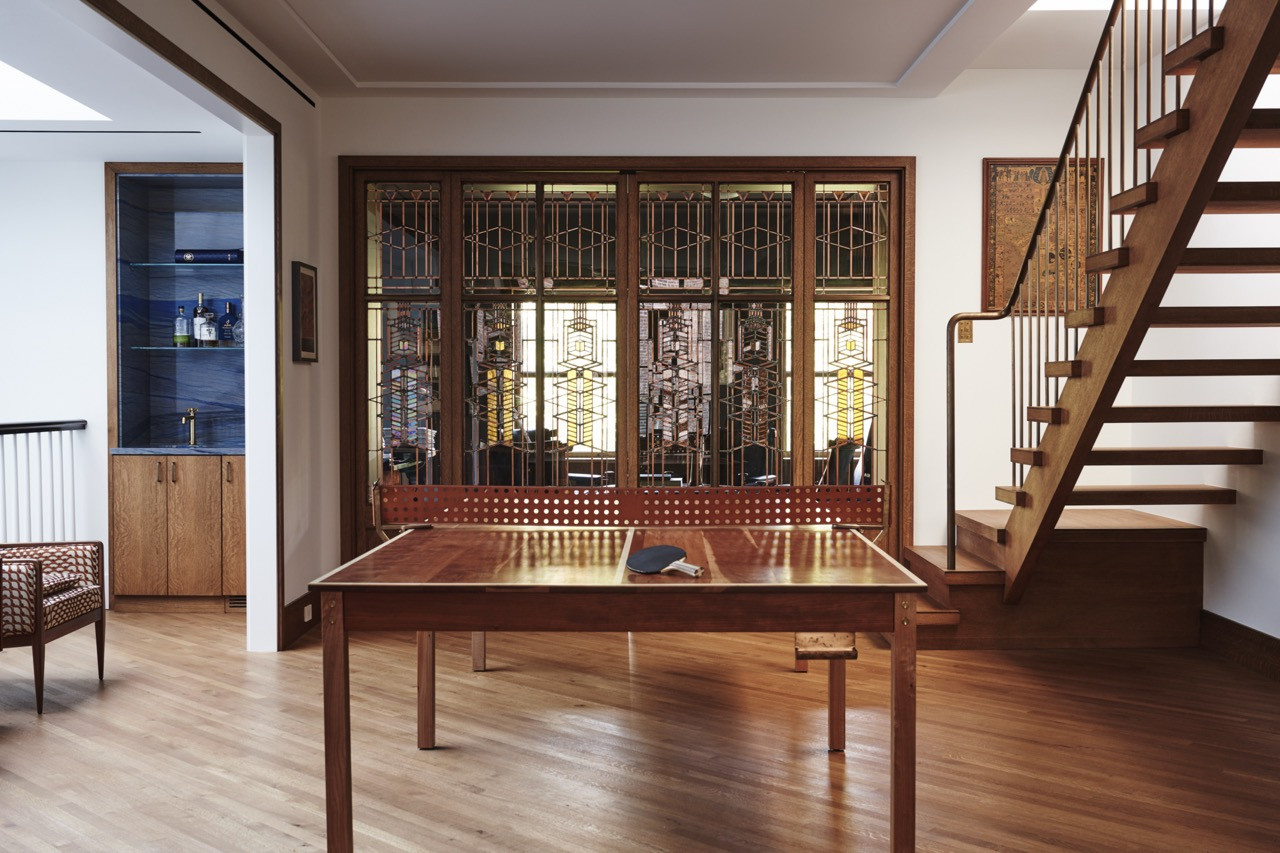 A ping-pong table set beneath a run of leaded-glass doors, with a bar nook and stairs to one side