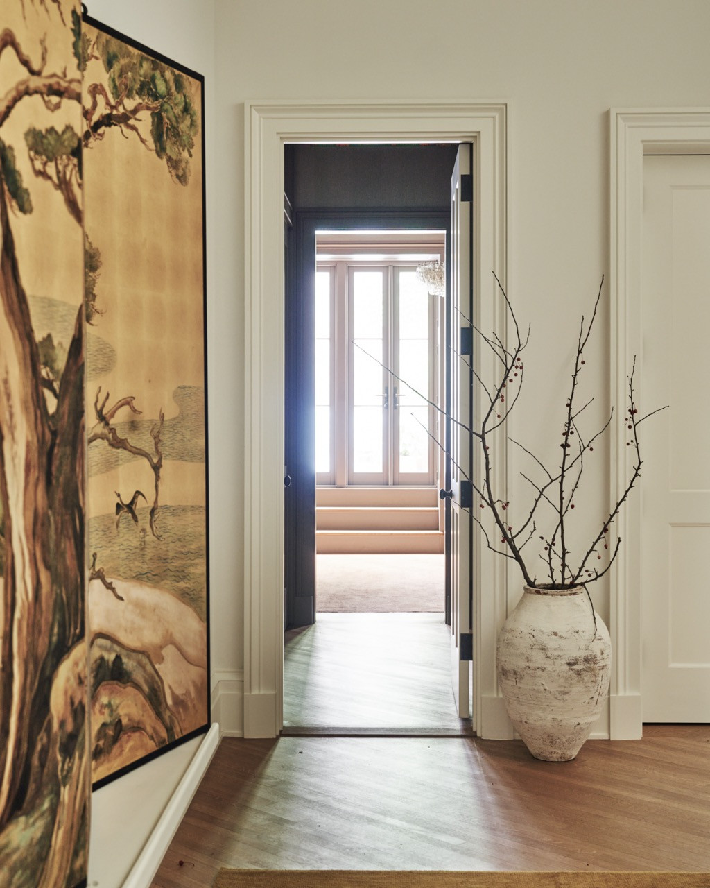 A hand-painted screen depicting trees and cranes, glimpsed beside an open doorway leading toward a sunlit room