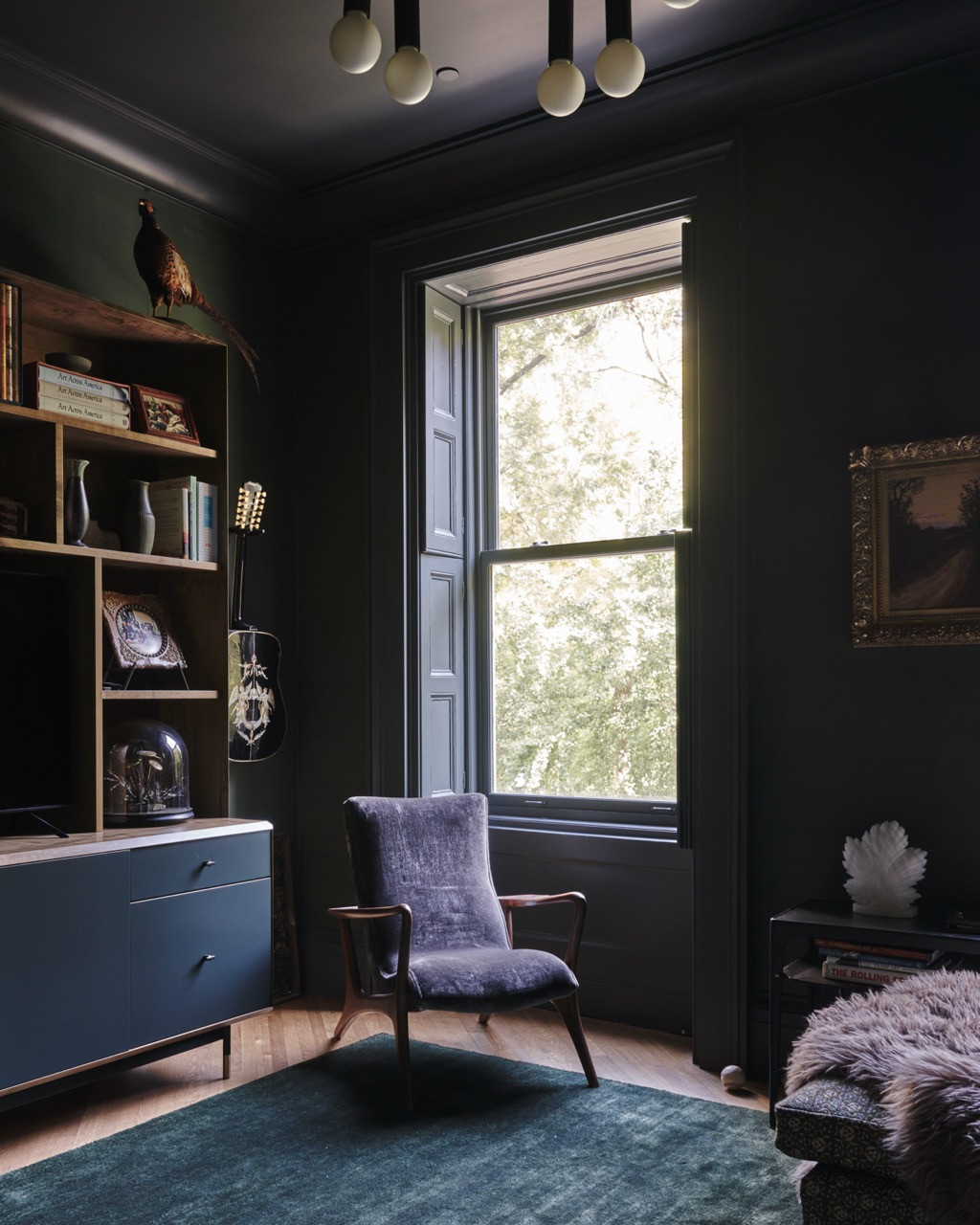 A study or den in deep charcoal tones, with a taxidermy pheasant, a guitar, and a velvet armchair by the window