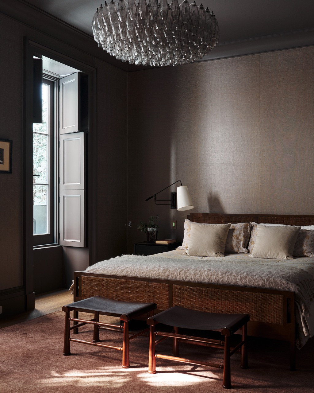 A bedroom in muted, tonal browns, with a cane bed frame and a cluster of glass pendant lights overhead