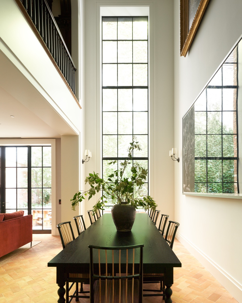 The double-height atrium linking the garden-level kitchen to the dining room above, framed by the tall steel-and-glass window facing the rear garden