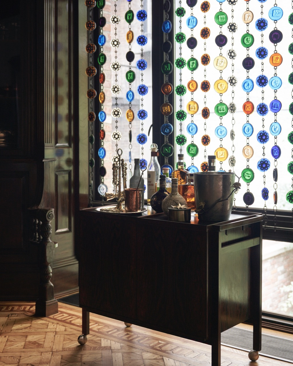 A beaded glass curtain filters light over a small bar cart stocked with spirits and barware