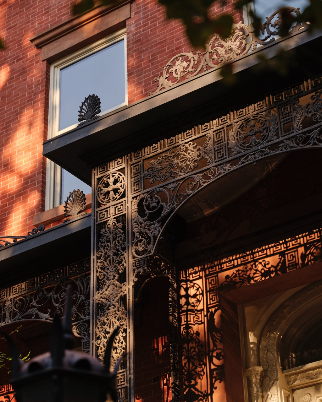 A close view of the ironwork bracket and fretwork above the entrance, its Greek key and scroll motifs catching the late-day light