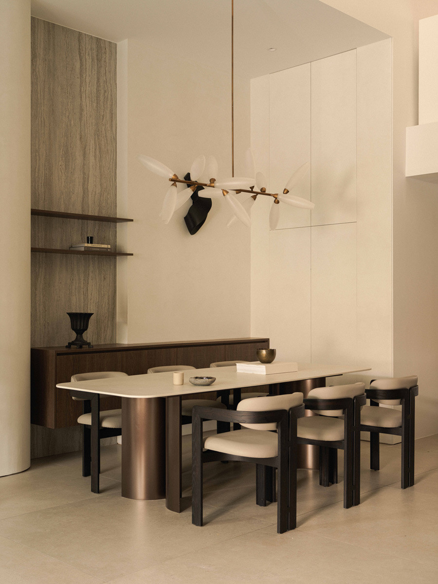 A custom dining table with curved metal legs and a Dekton surface stands beneath a sculptural chandelier in the terrace house’s dining room