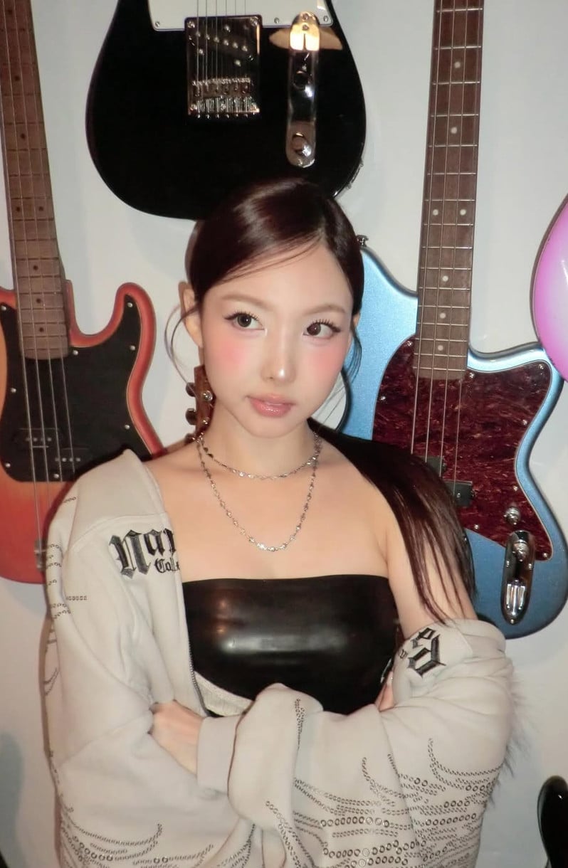 TWICE's Nayeon poses in a black top and light hoodie, with electric guitars visible in the background.