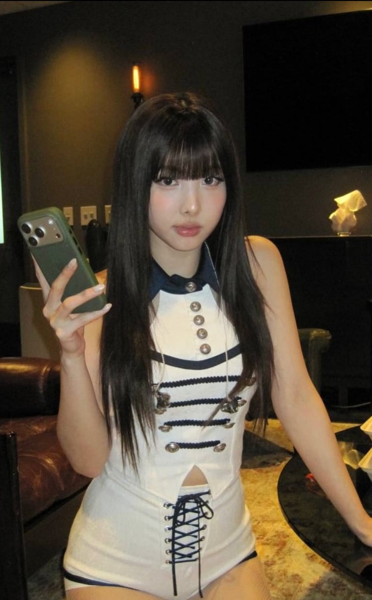 K-pop artist Nayeon sports a white and navy, sailor-inspired ensemble with a smartphone in hand.