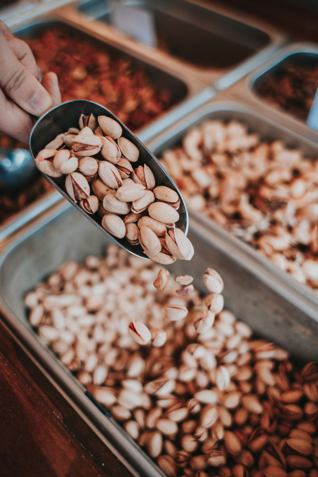 Roasted pistachios are scooped from a bulk bin, offering a satisfying snack or culinary ingredient.