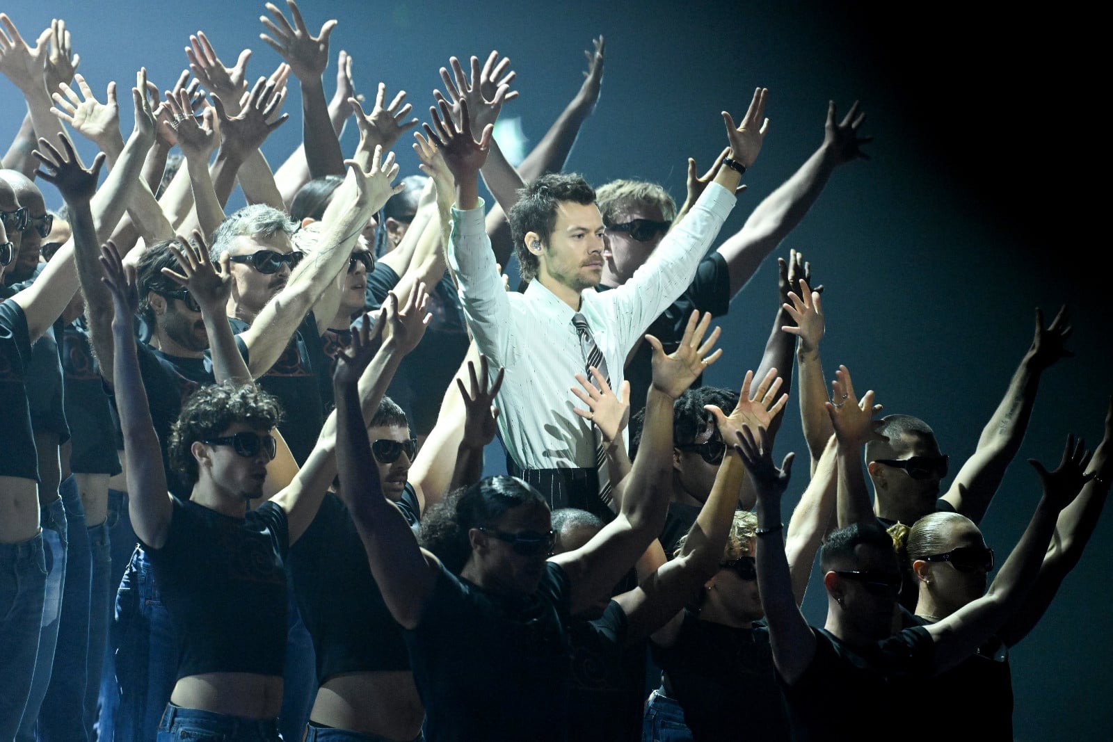 Harry Styles performs alongside an ensemble of dancers with raised hands.