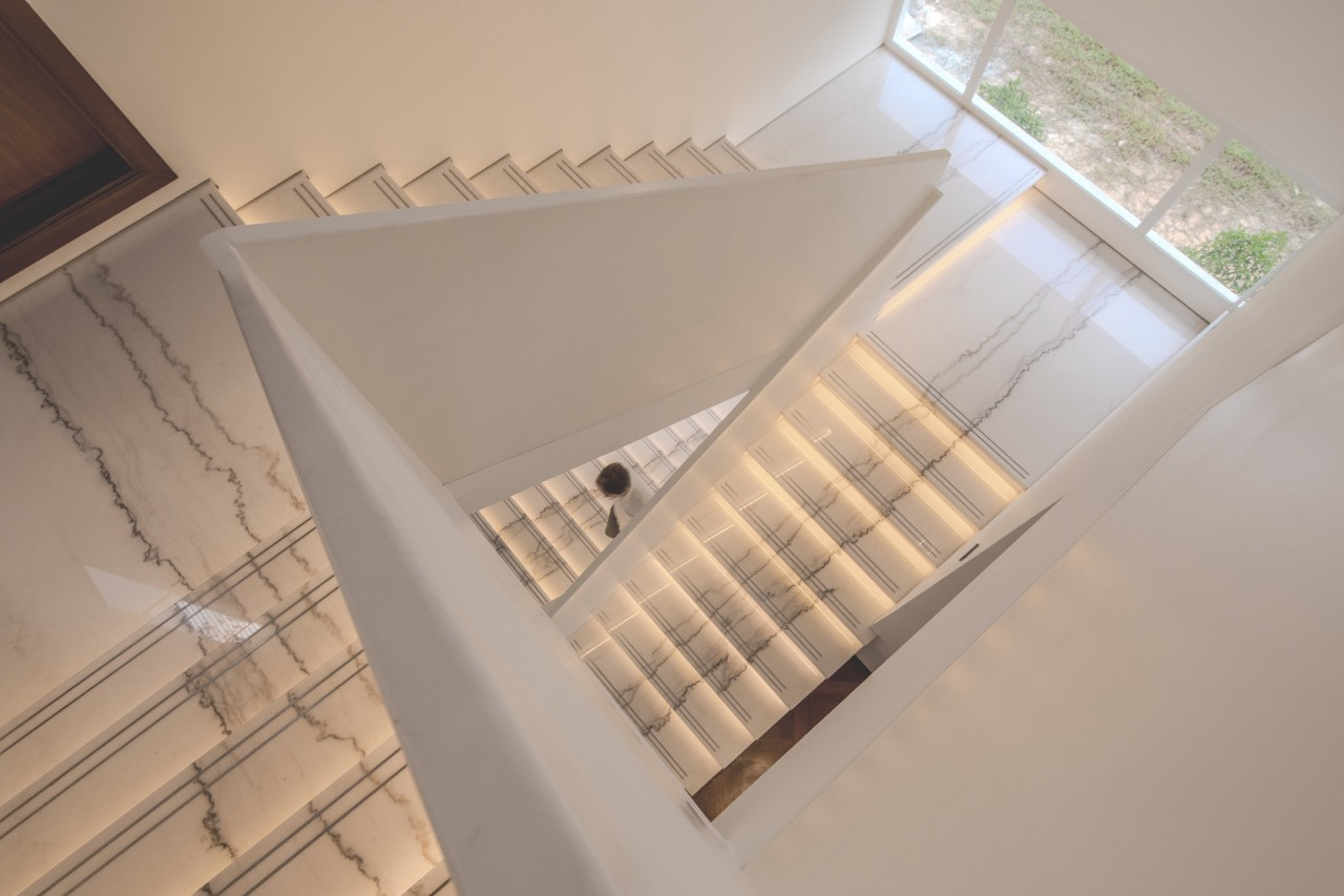 The stairwell is lit from above by a clerestory skylight that changes the pattern of light and shadow across the stairs throughout the day