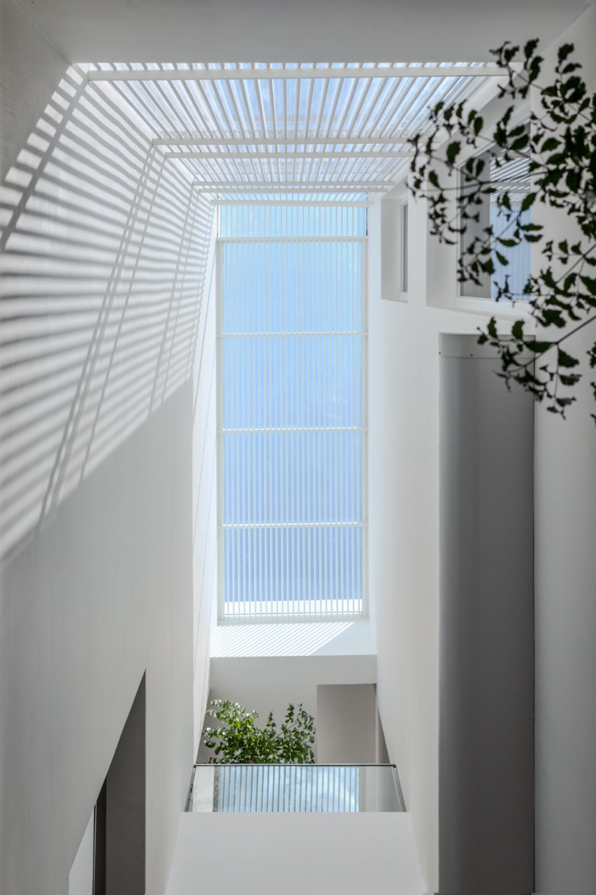A light well above the stairwell, where a louvred roof casts moving bands of shadow through the interior