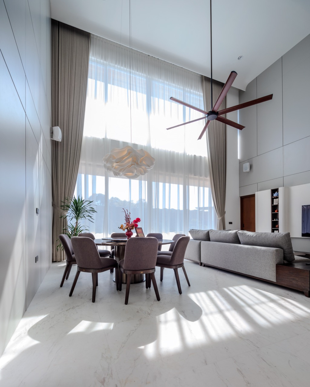 A round dining table sits beneath the same tall glazing that runs the length of the ground floor living spaces