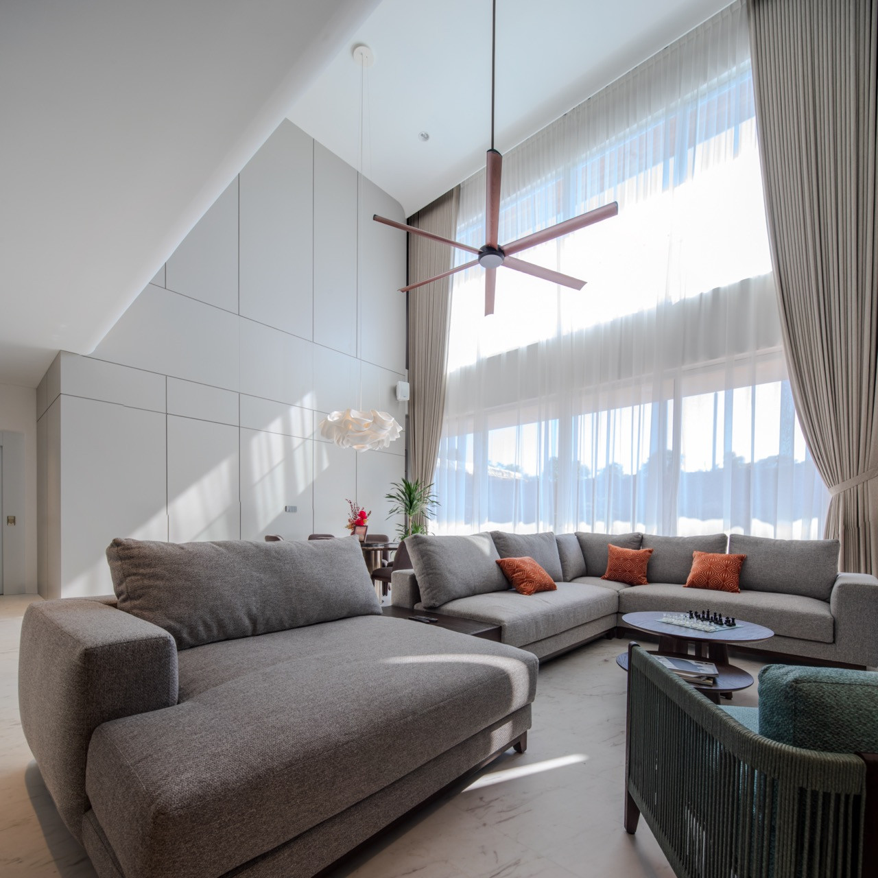 The main living hall, defined by a double-height ceiling and a wall of sheer curtains that filter the afternoon light