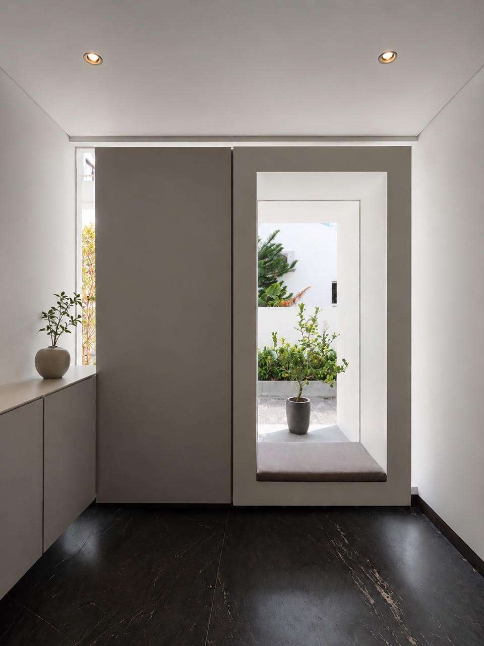 A quiet entry nook with a built-in bench seat and a window framing a single potted tree