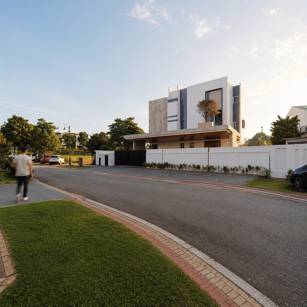 The house, seen from the street, has layered white and concrete volumes set back behind a low perimeter wall
