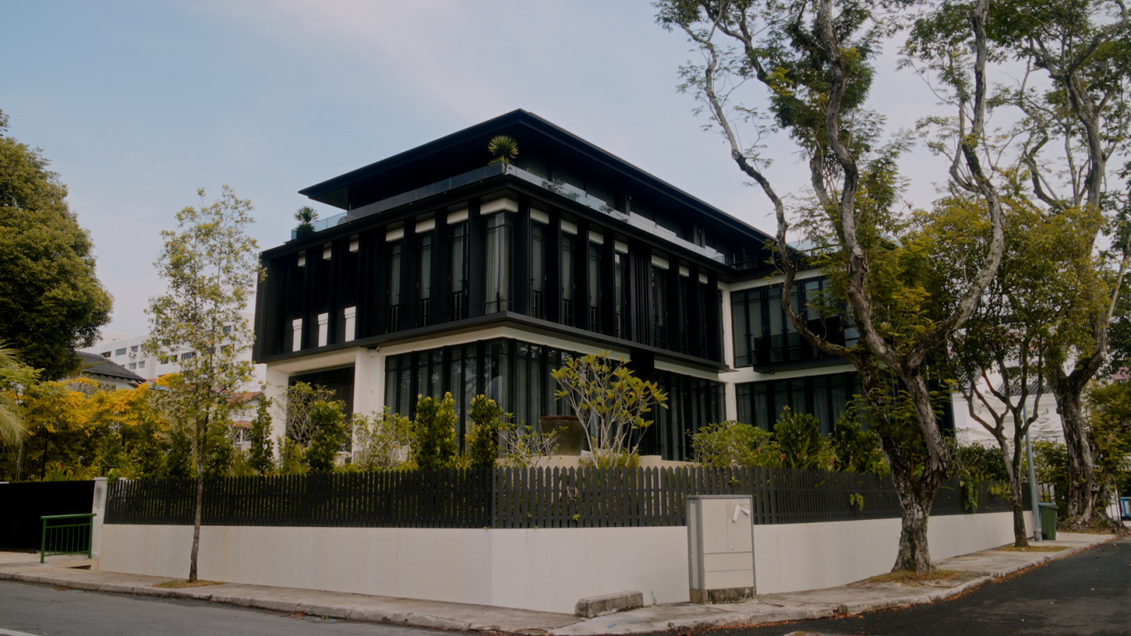 The bungalow’s dark, crisp facade rises above its corner plot in District 10, framed by mature street trees and young planting that will soon grow into a green screen