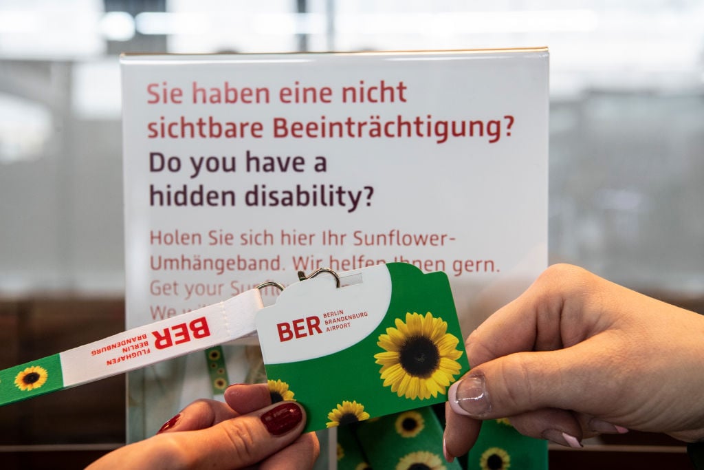 Brandenburg, Schönefeld: A BER Airport employee hands a "Sunflower" card with lanyard to a traveler. BER is the first German airport to introduce the "Sunflower" program to support people with non-visible impairments. Photo: Paul Zinken/dpa (Photo by Paul Zinken/picture alliance via Getty Images)