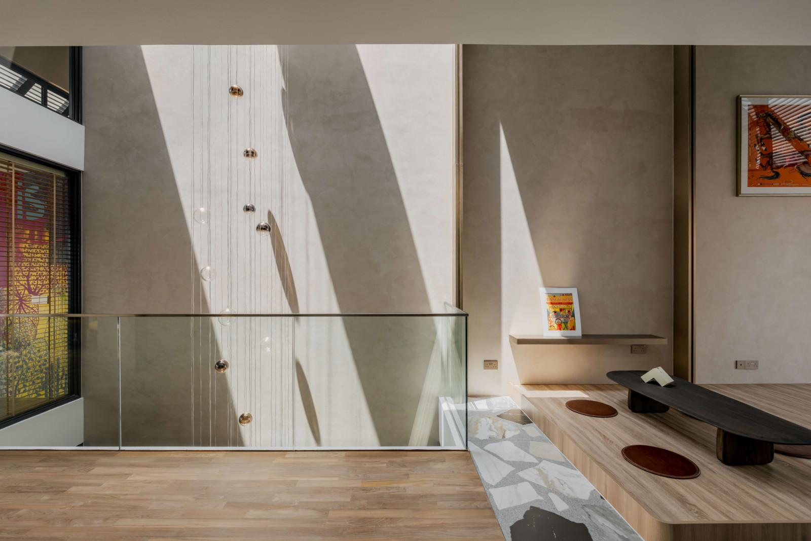 A sculptural pendant light hangs through five storeys from the skylight, connecting the different levels vertically, while suspended artwork extends through the void and becomes visible from multiple spaces