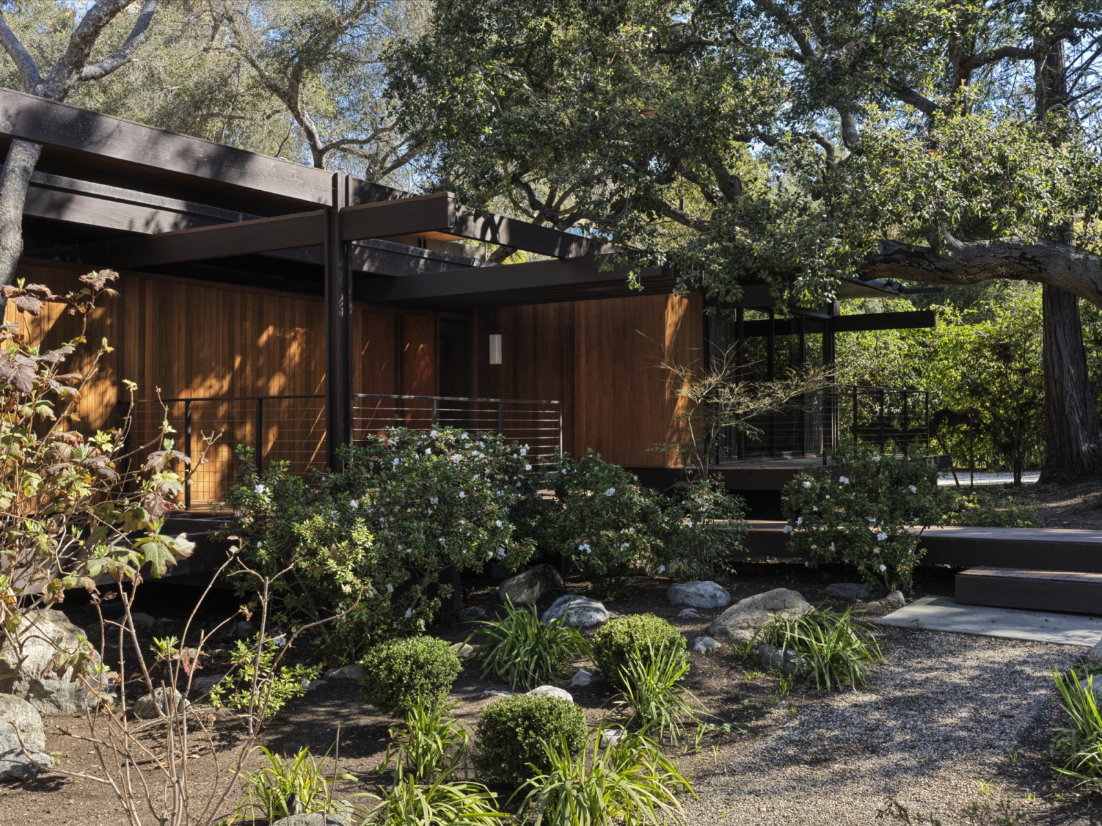The street-facing facade of the residence with a bridge path and multi-level entry patio in hardwood decking of a California home designed by Kate Driver of West Haddon Hall
