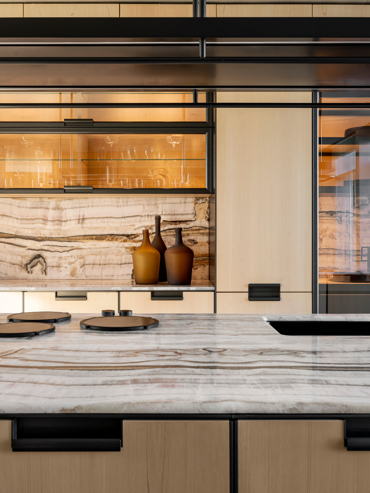Integrated warm LED lighting concealed within the cabinetry, transparent glass doors and open compartments