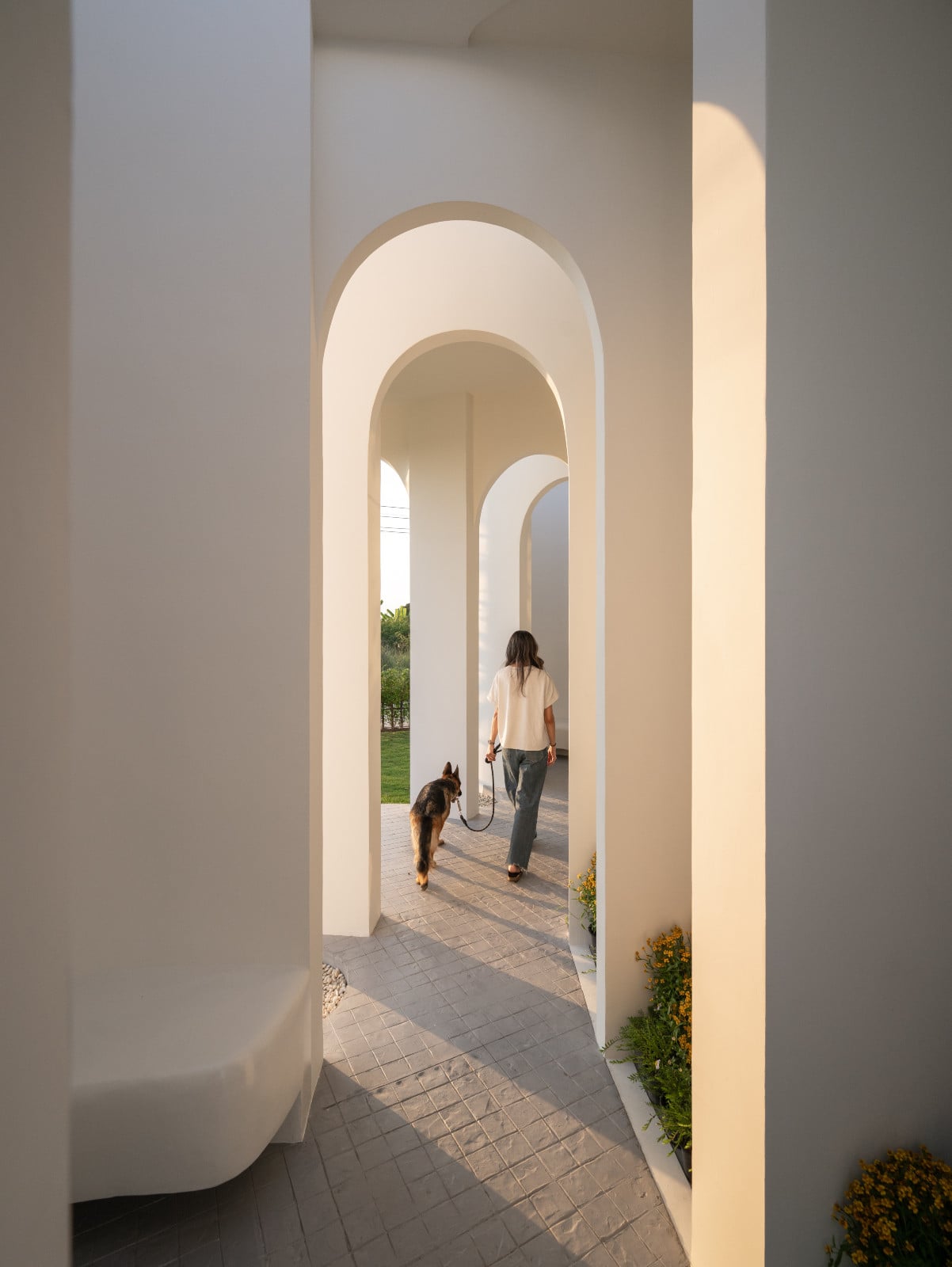 ทางเดินกึ่งเอาต์ดอร์ (Semi-outdoor) ที่เกิดจากเทคนิคการเจาะคว้าน (Subtractive Design) แสงเงาที่พาดผ่านกรอบโค้งสร้างจังหวะการเดิน (Slow Reveal)