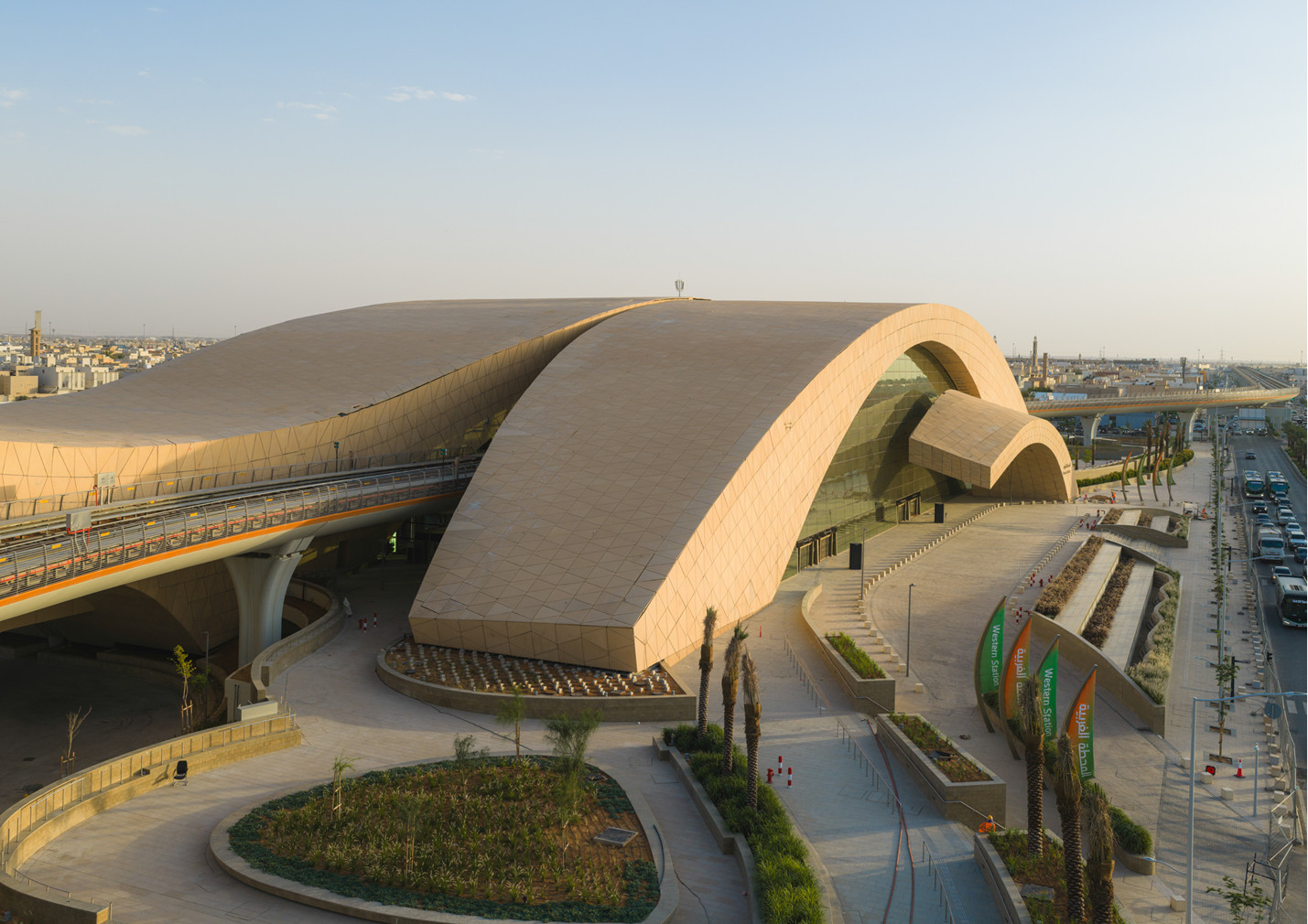At dusk, two arches clad in faceted sand-coloured panels frame the main entrance of Western Station in Riyadh (Photo: Omrania)