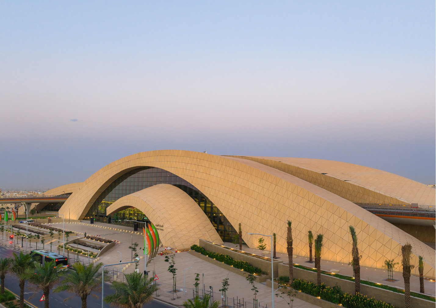 At dusk, two arches clad in faceted sand-coloured panels frame the main entrance of Western Station in Riyadh (Photo: Omrania)