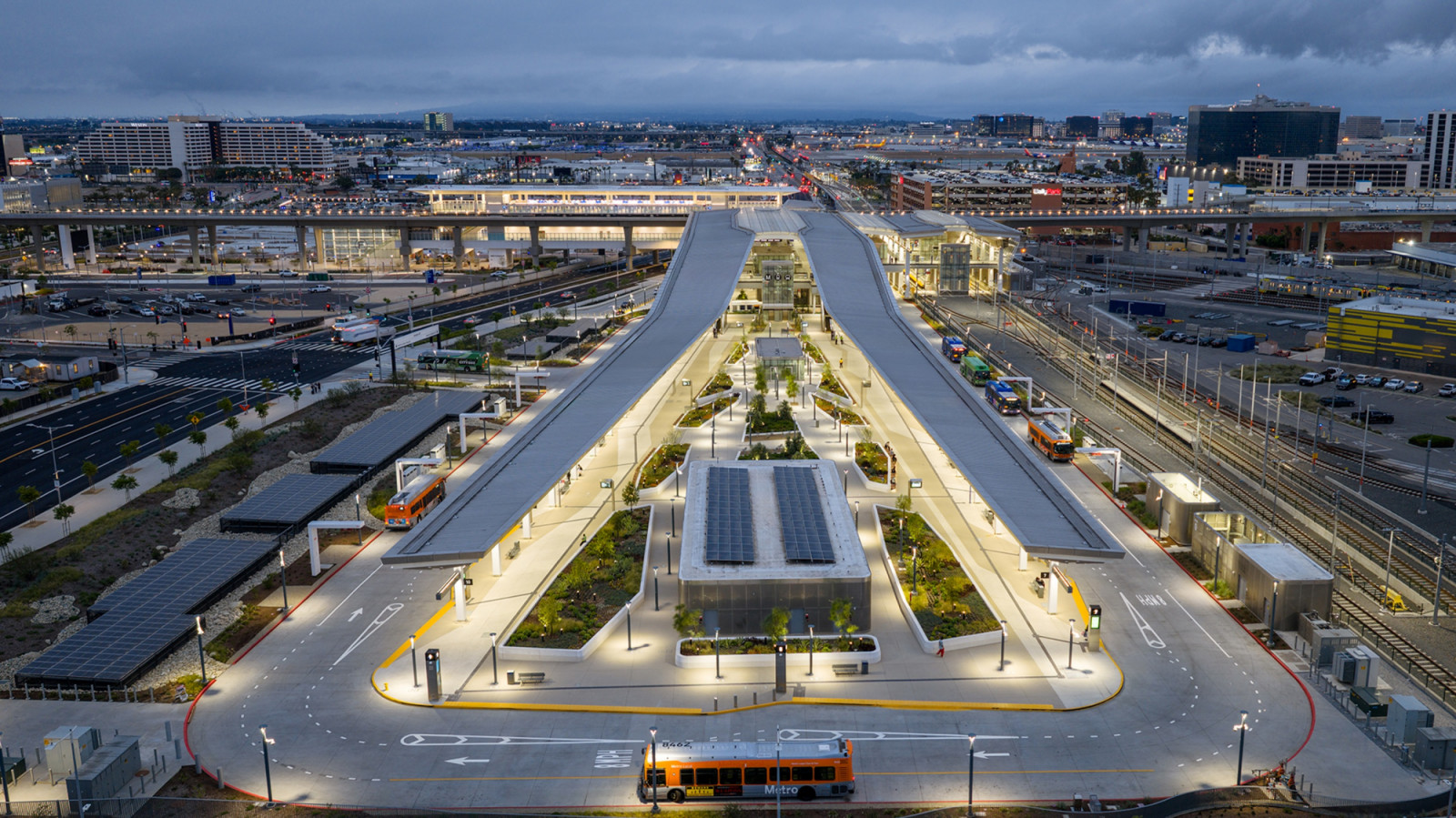 At dusk, solar panels cover the roof of a central pavilion in the bus plaza of the LAX/Metro Transit Center, between two long, lit canopies (Photo: Jason O’Rear)