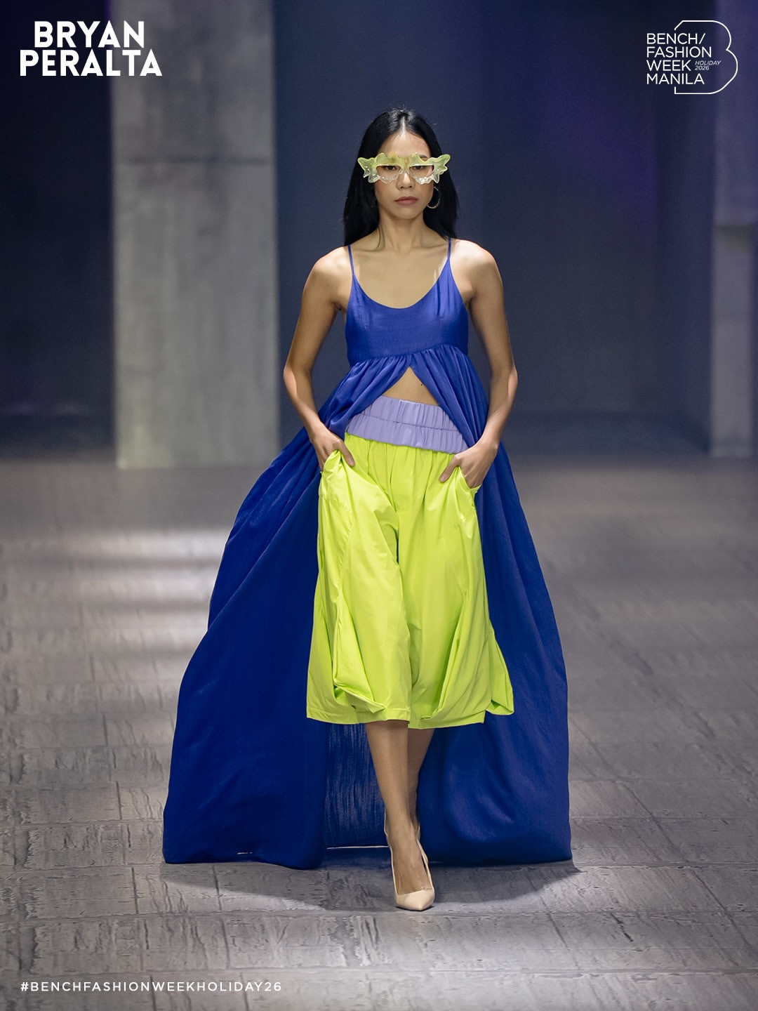 A model presents Bryan Peralta's blue dress and neon green bubble trousers from the Bench Fashion Week Holiday 2026 collection