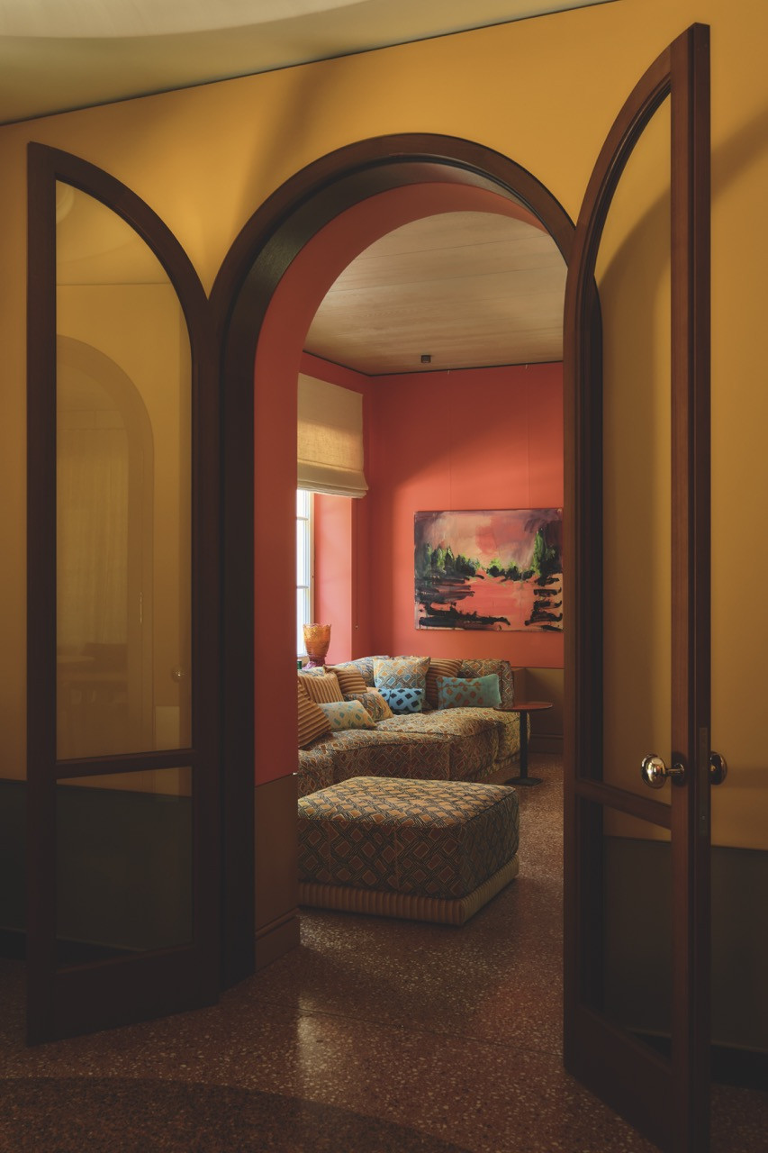 An arched doorway opens from the yellow hall into a coral-walled sitting room