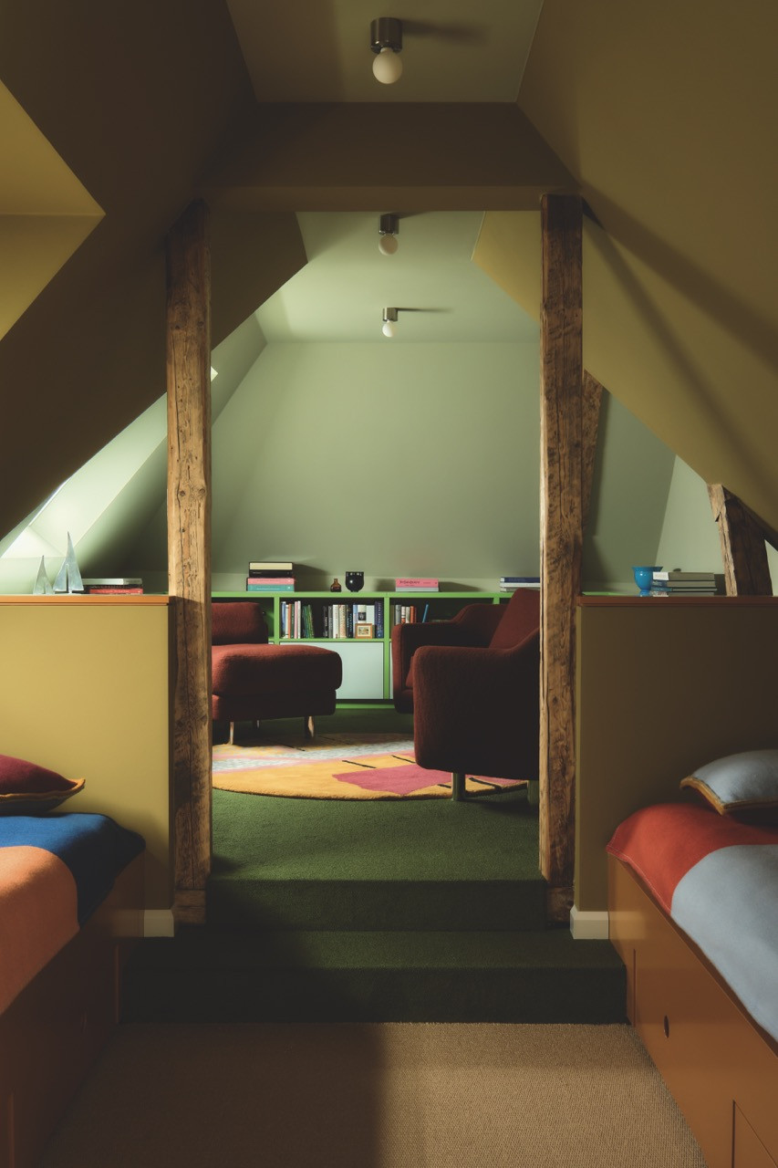 Reclaimed beams frame a sitting area furnished with burgundy armchairs in the attic