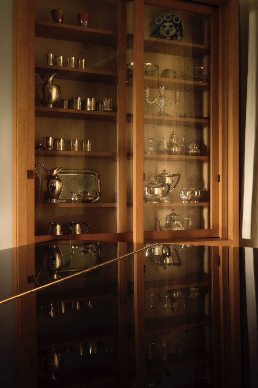 A glass-fronted cabinet displays a collection of silverware and glassware