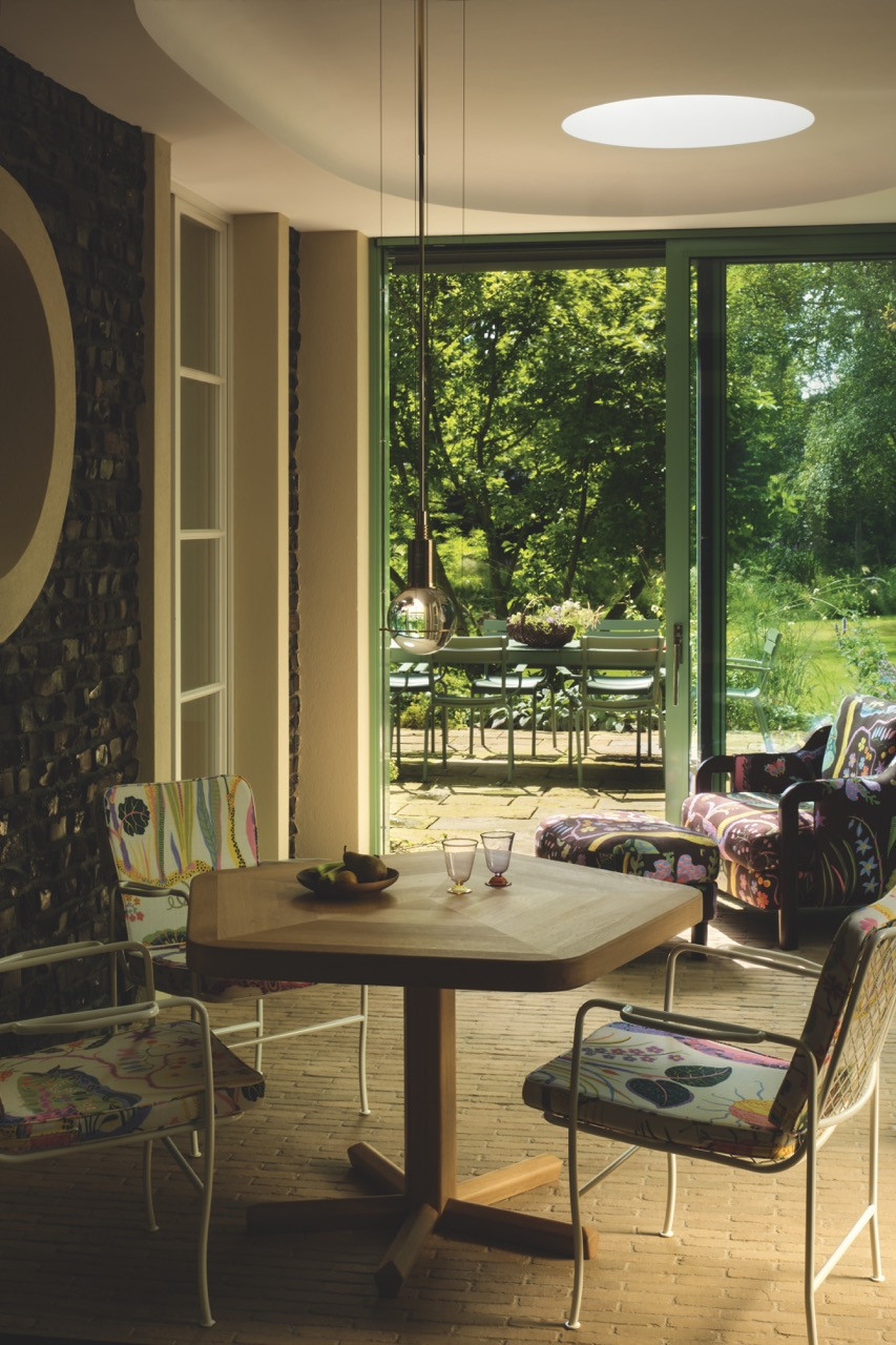 A wooden table in the garden room opens onto the terrace and lawn beyond