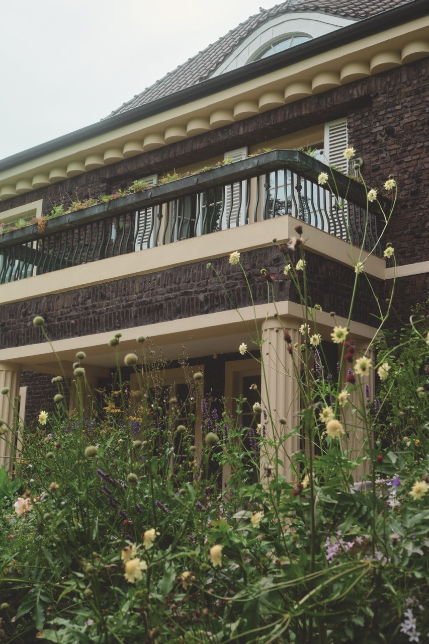 Wildflowers climb toward the villa's balcony and clinker brick façade