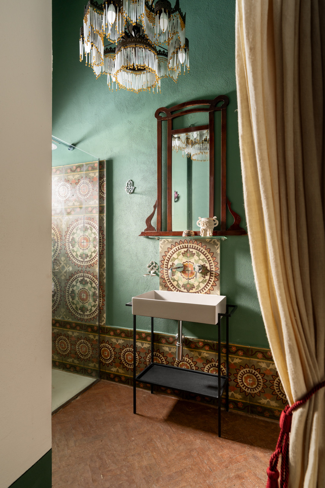 Reclaimed encaustic tiles are used for the basin backsplash alongside a tasselled chandelier and Art Deco mirror
