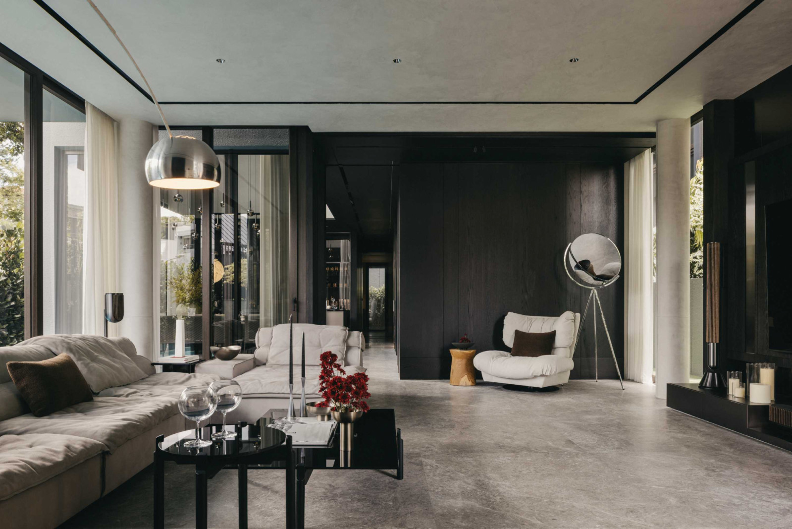 A dark timber wall anchors the living room, paired with a sculptural lamp and a swivel chair