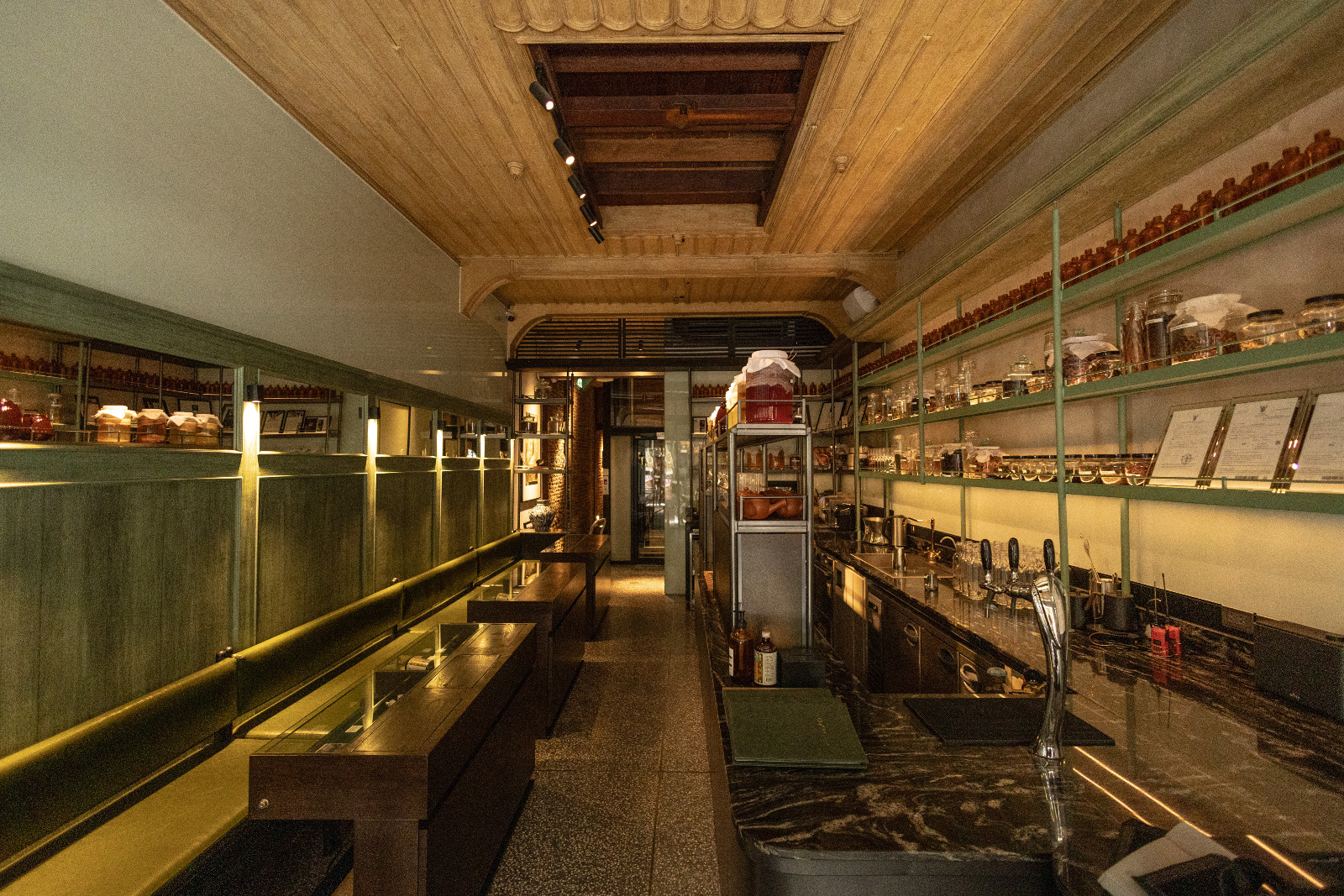 บรรยากาศชั้น 1 ที่ตีความความทรงจำของร้านขายยาจีนเดิม ผ่านเคาน์เตอร์ไม้ โทนสี Industrial Green และชั้นวางขวดยาโบราณ (ภาพ: Worapon Teerawatvijit)