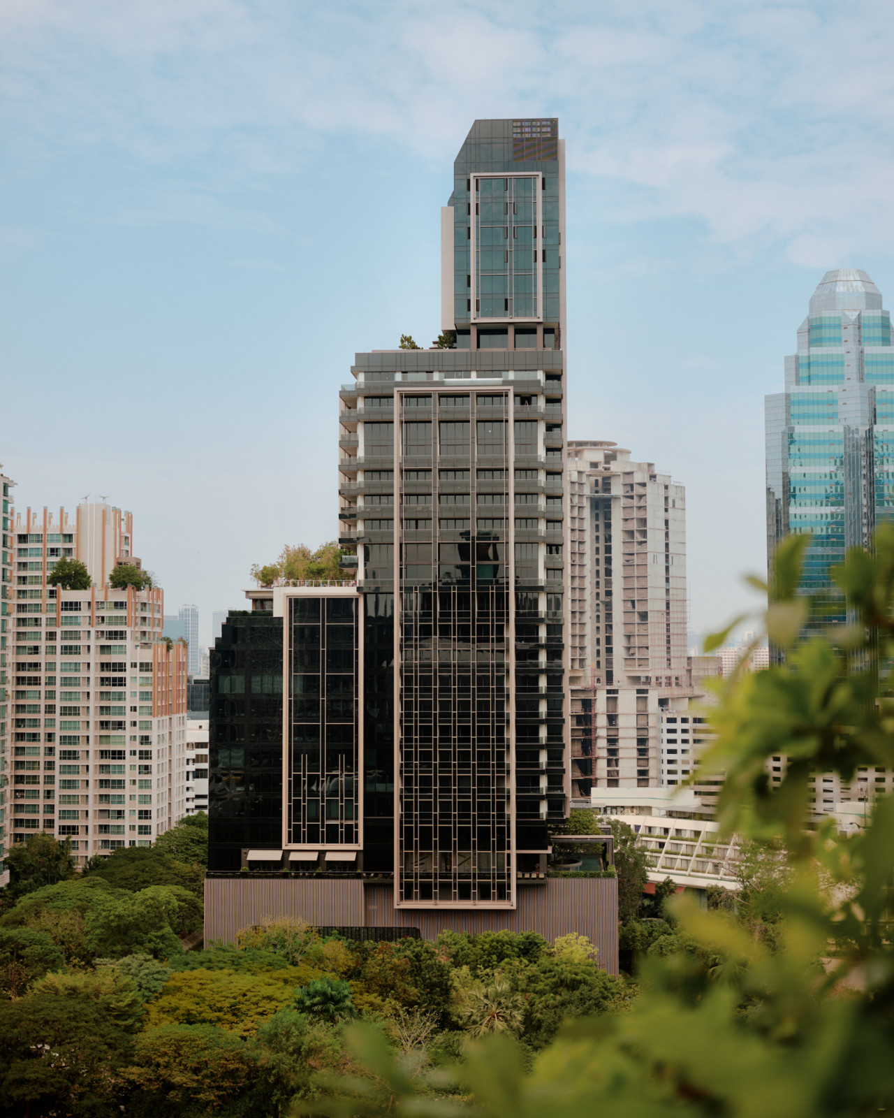 Seen across the treetops of Nai Lert Park, Aman Nai Lert Bangkok is defined by tall bronze-toned frames set against dark glass (Photo: Aman)