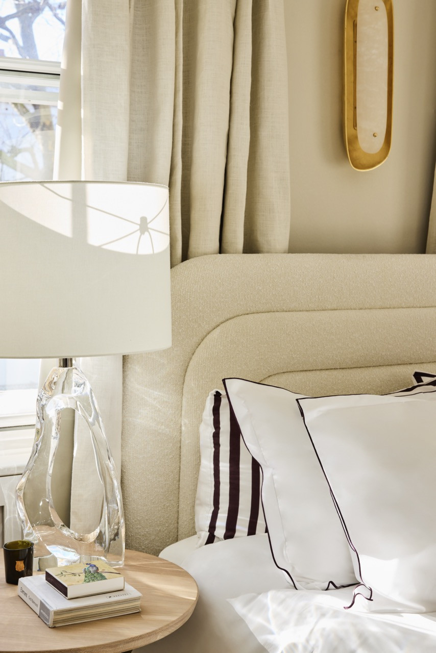 In the main bedroom, a sculptural glass lamp and a brass-and-alabaster wall light sit beside a curved bouclé headboard