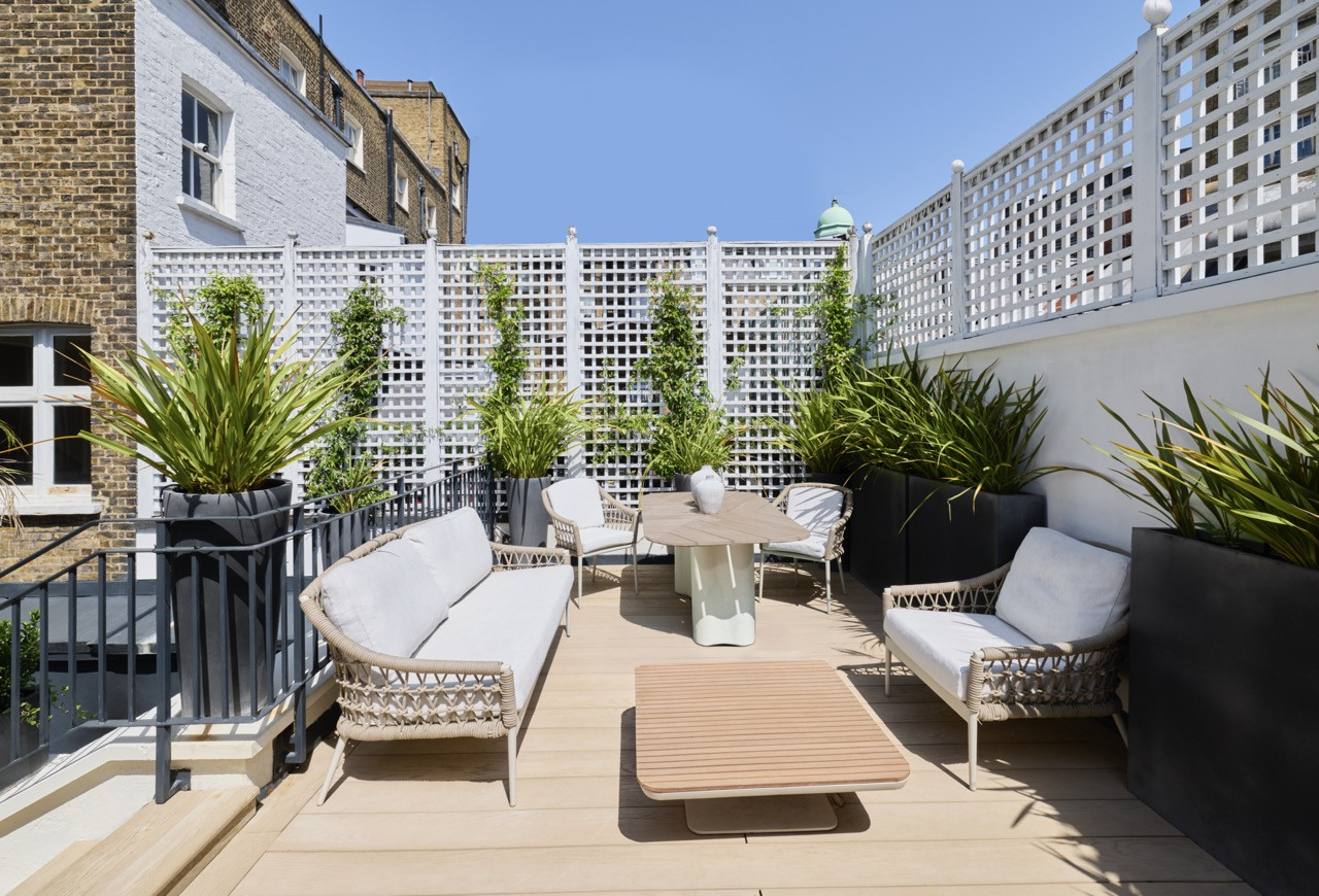 The rebuilt terrace, now laid with new decking, holds a lounge and dining area with woven outdoor furniture.