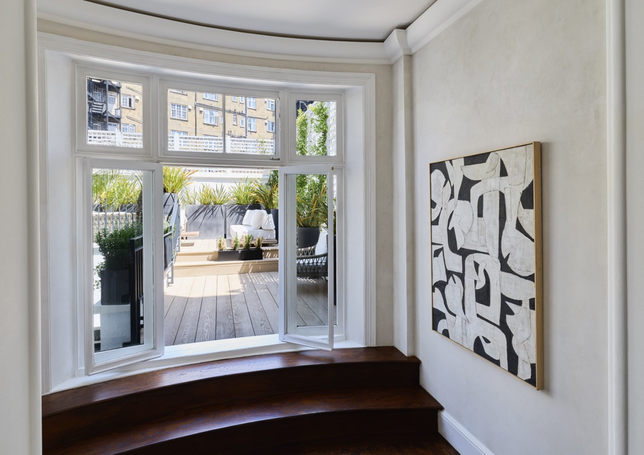 A bay window on the landing opens onto the terrace, beside a black-and-white abstract canvas