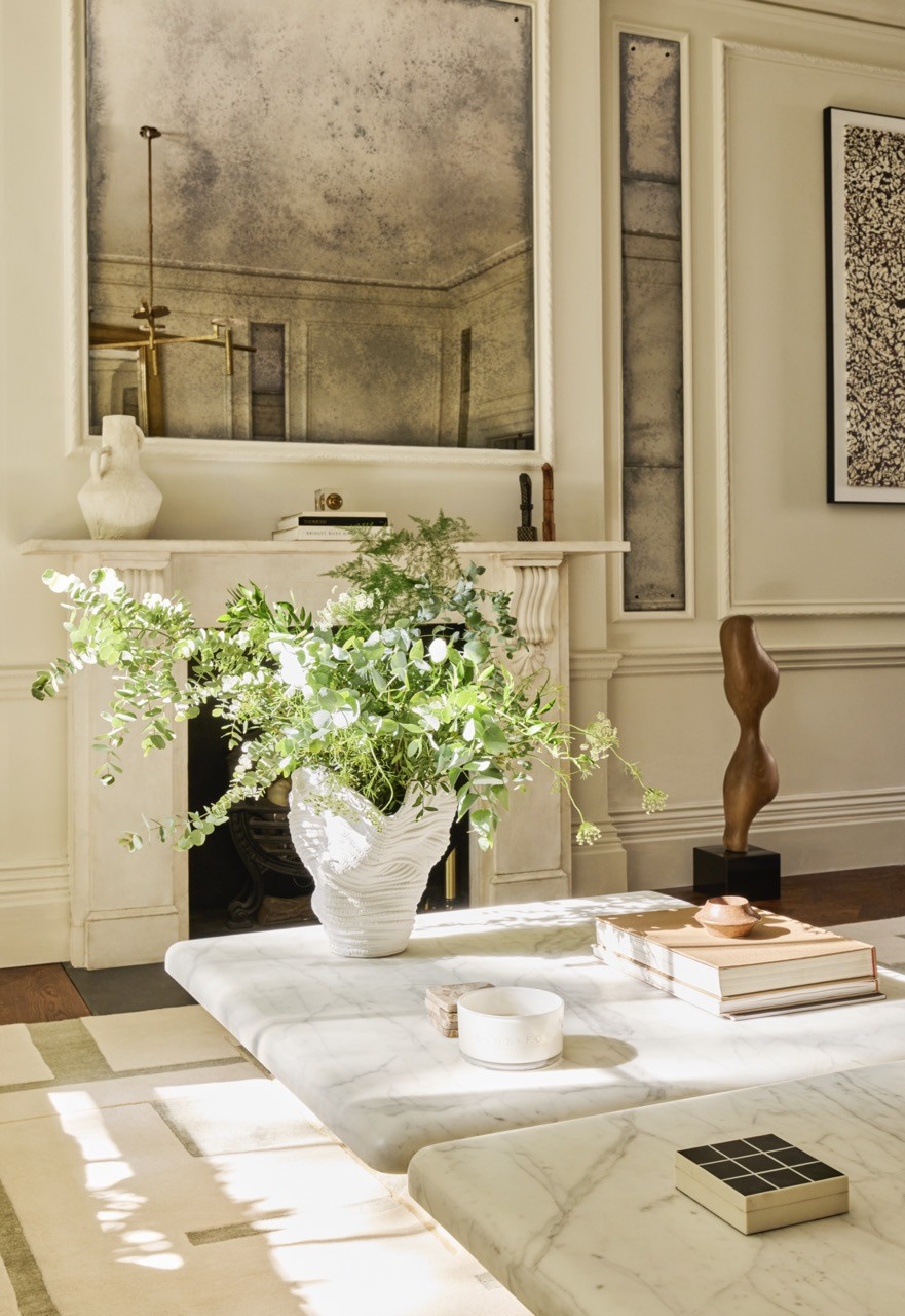 A sculptural white vase and a carved wooden sculpture sit before the original marble fireplace and antiqued mirror in the living room