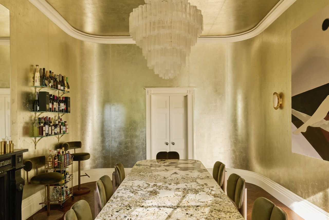 In the dining room, a tiered glass chandelier hangs over a marble table, with a bar built from Amazon brackets and shop-cut glass
