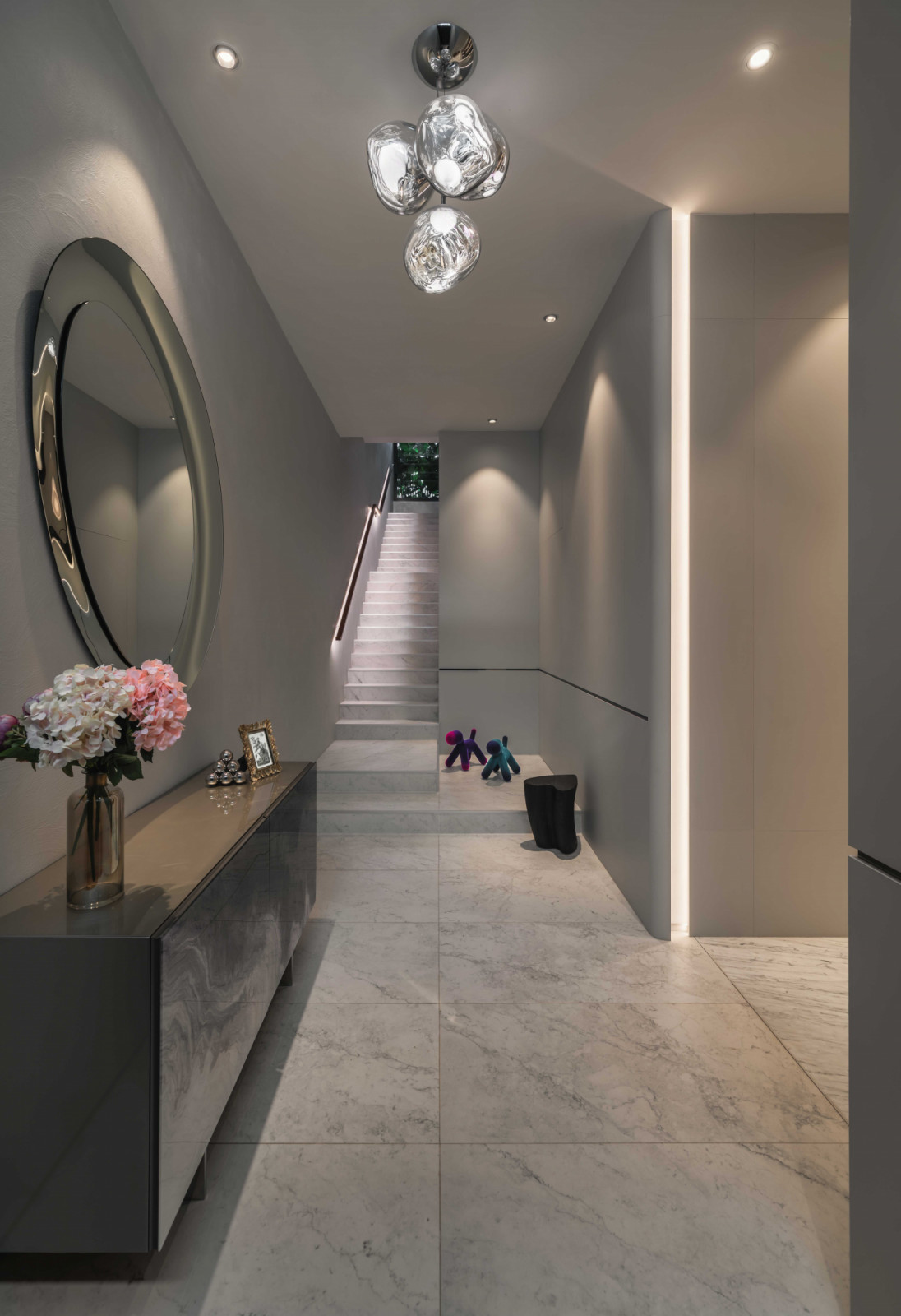 Softly illuminated by linear lights and sculptural crystal pendants, the entrance hallway welcomes visitors