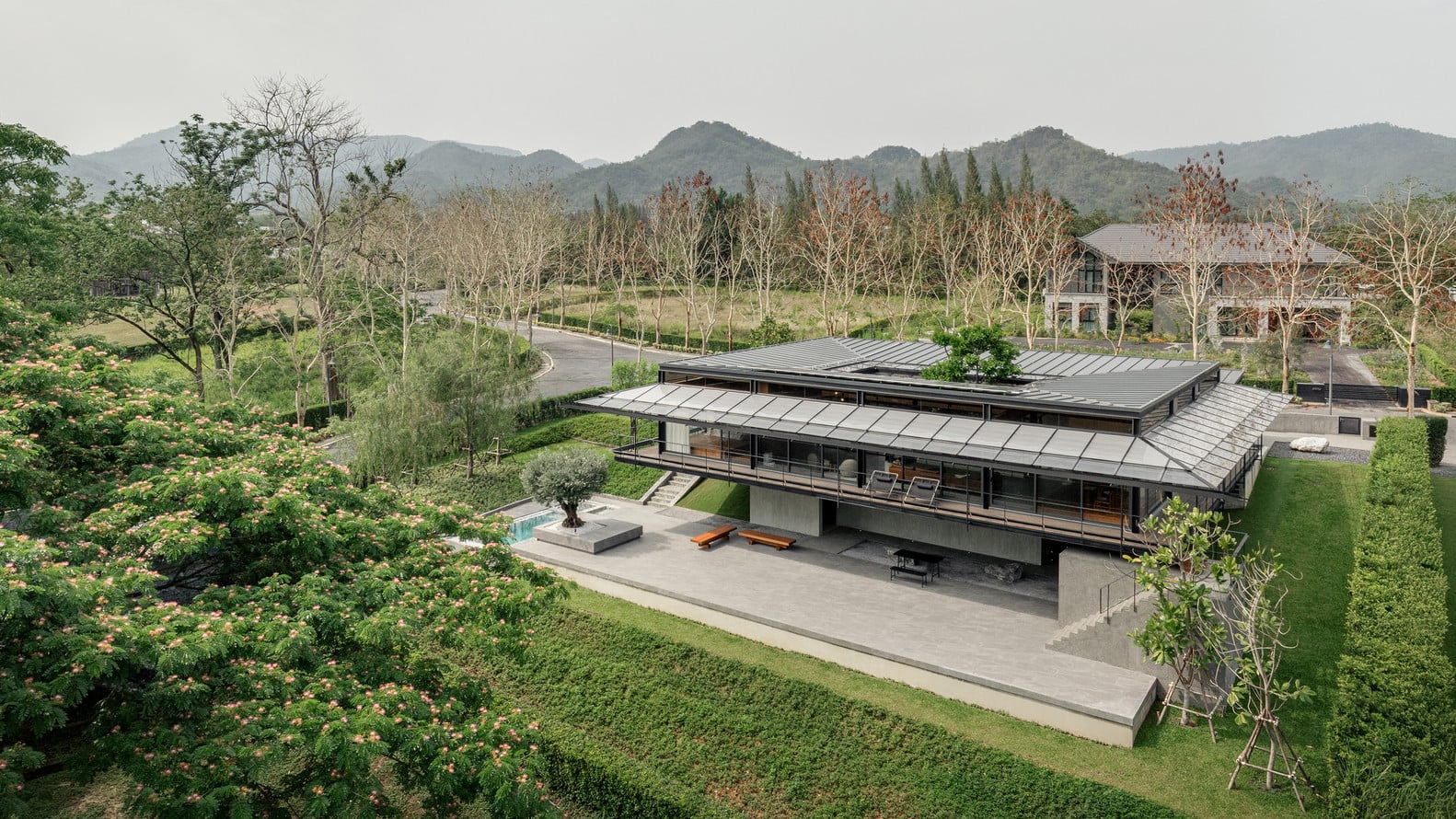 Baan O+O ที่โอบล้อมด้วยขุนเขา โดดเด่นด้วยโครงสร้างหลังคาที่เปิดช่องว่างให้ต้นไม้จากคอร์ตยาร์ดกลางบ้านเติบโตขึ้นมา (ภาพ: DOF Sky|Ground)