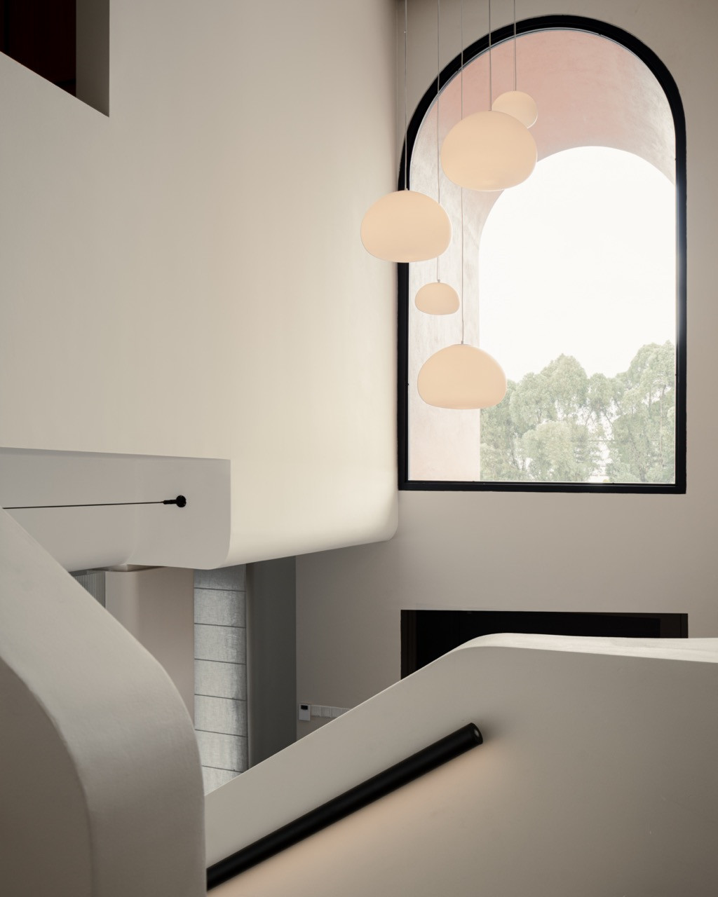 Pendant lights hang in the double-volume stairwell, in front of the arch-shaped glass panel set into the terracotta façade