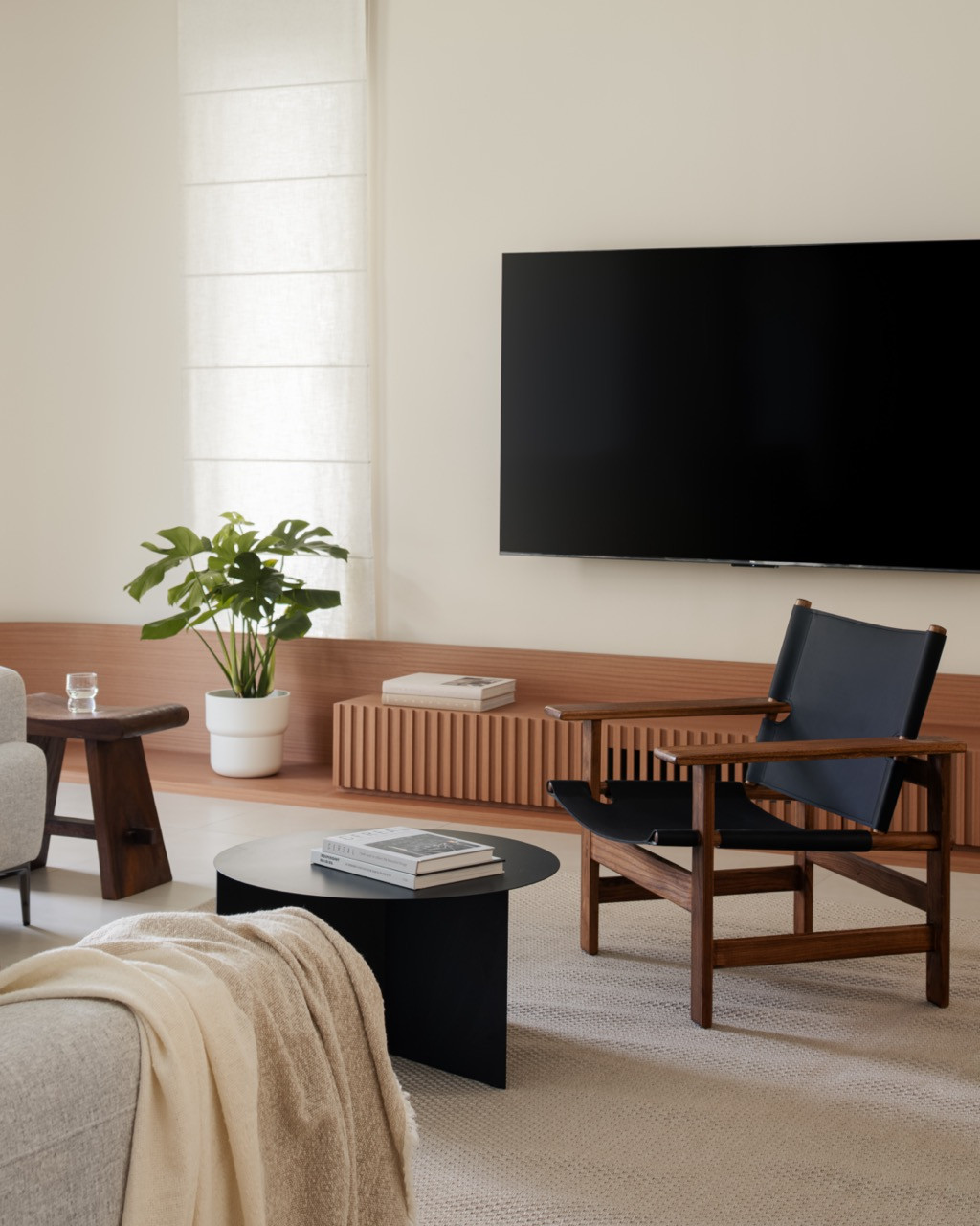 In the living room, a Hay coffee table and a leather sling chair face a low fluted console in wood-look laminate